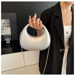 Silver acrylic crescent clutch bag shown in a modern home setting with a gold chain strap