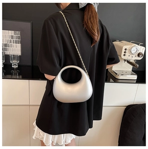 Silver crescent acrylic handbag with elegant gold chain strap shown on model's shoulder
