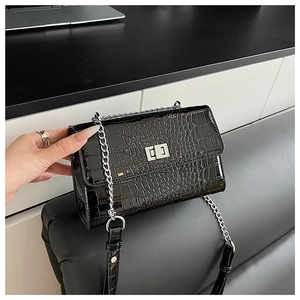 Close-up of black crocodile pattern leather bag with silver metal lock and chain strap