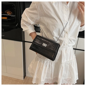 Model wearing a black croc-effect crossbody bag with silver twist lock and chain strap