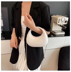 Chic white crescent acrylic clutch with golden chain strap shown in a lifestyle setting