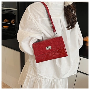 Detail of red crocodile texture crossbody bag with silver lock and chain strap on a model