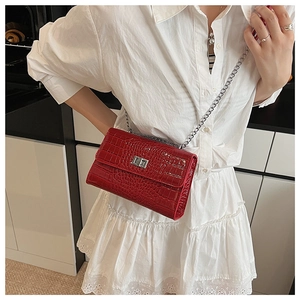 Detail of red croc-embossed texture and silver metal chain on a glossy crossbody bag
