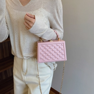 Pink quilted hard shell crossbody bag with gold chain strap and top handle in casual setting