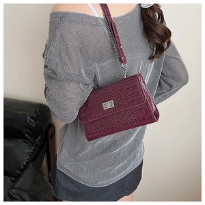 Detail of wine red crocodile embossed leather shoulder bag with silver turn-lock clasp