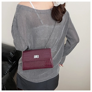 Detail of burgundy crocodile-embossed bag with silver chain strap and metal clasp