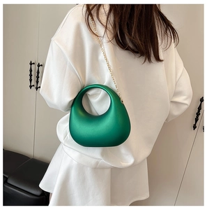 Rear view of a model carrying a green crescent evening bag with a gold chain strap