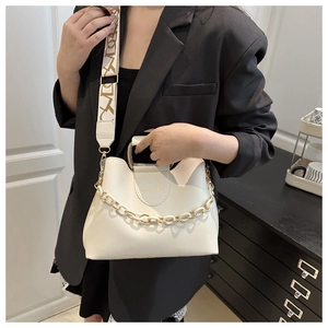Detail of cream bucket bag featuring wavy rim, golden chain, and wide printed strap