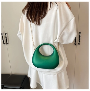 Detail of emerald green half-moon acrylic evening bag with gold chain strap on model