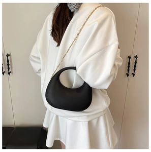 Detail of a minimalist black crescent acrylic evening bag with a gold chain strap link