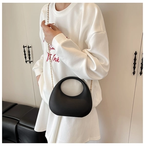 Detail view of the sleek black crescent handbag with a unique cutout handle and gold chain