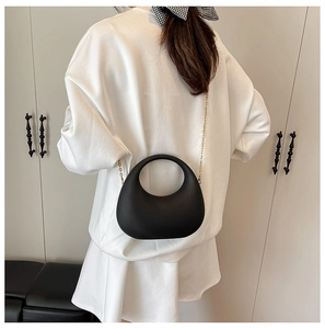 Detail of matte black crescent bag with hollow handle and gold chain on white outfit