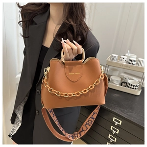Detail view of brown bucket bag with gold handle, thick chain and blue printed shoulder strap