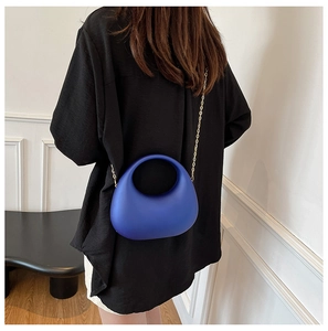 Detail of blue acrylic crescent handbag with gold chain strap shown on a model