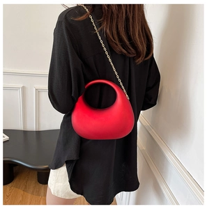 Detail view of red acrylic crescent evening bag with gold chain strap worn by a model