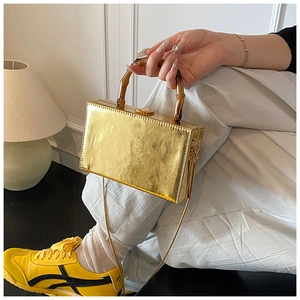 Close-up of golden box bag with vintage bamboo top handle and elegant metal chain strap