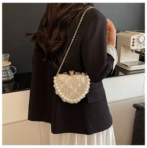 Close-up of heart-shaped lace evening bag with pearl trim and gold chain on woman back