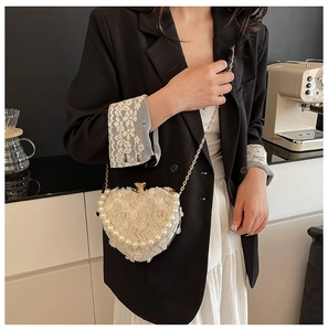Detail view of heart shaped lace bag with pearl trim and gold chain on model