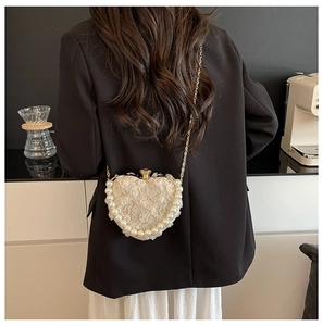 Detail of heart-shaped lace bag with pearl trim and gold chain shown on a model