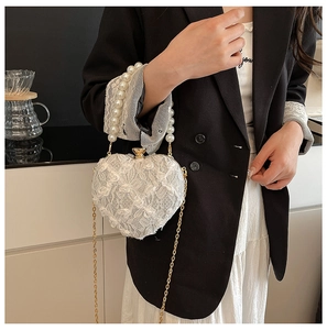 Detailed view of heart-shaped lace evening bag with pearl handle and gold chain strap