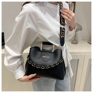 Detail of black bucket bag featuring golden hardware and wide patterned fabric strap