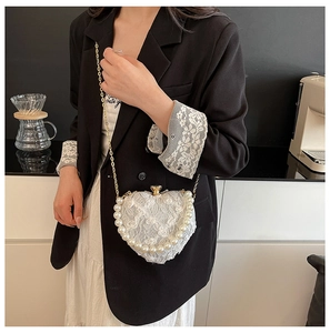Detail of heart-shaped white lace bag with pearl trim and gold chain on a model