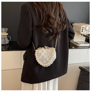 Detail of heart-shaped lace bag with pearls and chain on a black blazer backdrop
