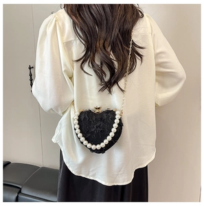Detailed view of heart-shaped lace evening bag with pearls worn by a model from the back