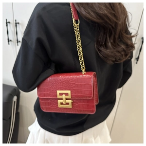 Detail van rode crossbodytas met krokodillentextuur, gouden gesp en kettingriem