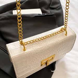 Detail van witte krokodillen tas met opvallende gouden ketting en vierkante metalen gesp