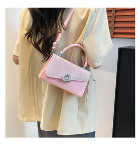 Detail of light pink sequin handbag featuring a metallic heart clasp and sleek handle