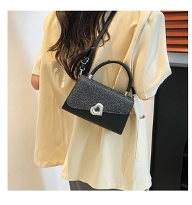 Detail of black sequined handbag featuring a silver heart buckle and chain strap