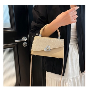 Detail of glitter sequins and heart-shaped metal lock on a beige crossbody square bag