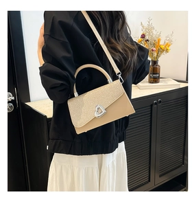 Detail of heart-shaped silver metal buckle and sequined flap on beige crossbody bag