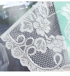 Detail of white lace cafe curtain with hollow floral patterns and scalloped edges