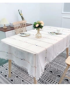 Detail of white cotton linen tablecloth with color stripes and white pom-pom fringe trim