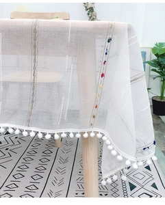 Detail of bohemian cream tablecloth with colorful stripes and pom-pom fringe