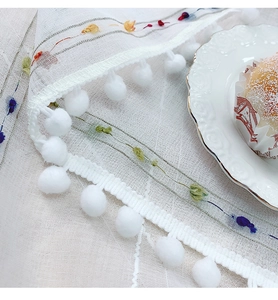 Detail of white semi-transparent tablecloth with floral embroidery and pom-poms