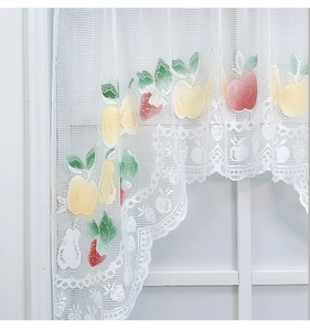 Detail of white lace kitchen curtain with fruit print and scalloped embroidery edge