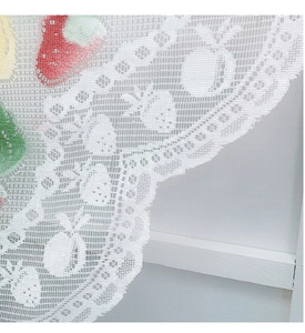 Detail view of white lace curtain with colorful fruit patterns and wavy scalloped edge