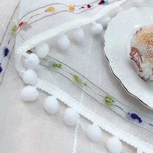 Modern white tablecloth with colorful floral embroidery and decorative pom-pom fringe trim