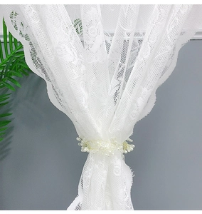 Detail of white lace door curtain featuring delicate floral patterns and pearl tieback