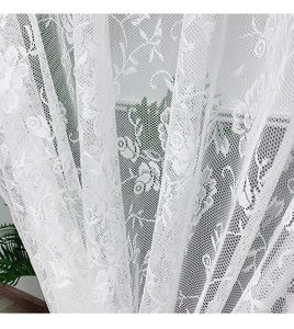 Detailed close-up of white lace curtain with intricate floral embroidery and mesh texture