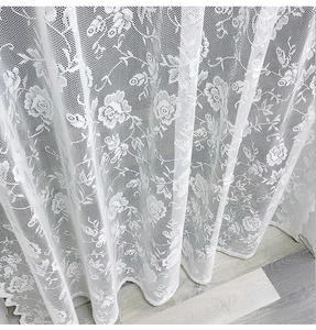 Close-up of white lace curtain featuring rose floral patterns and fine mesh texture