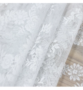 Close-up of white lace curtain fabric with delicate rose patterns and mesh texture