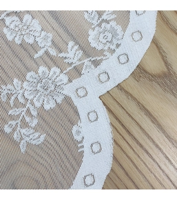 Detail of white lace curtain with floral embroidery and scalloped edges on wood background