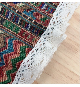 Close-up of colorful woven geometric pattern with white lace trim on a wooden table surface