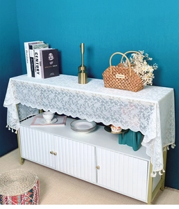 Close-up of white floral lace table runner with fringe tassels on a white console table