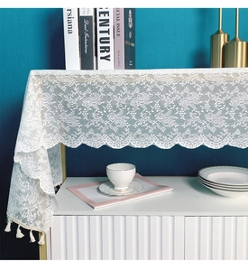 Close-up of white lace table runner with floral rose patterns and soft fringe tassels