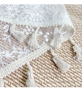 Close-up of white lace fabric with fringe tassels on a textured woven background